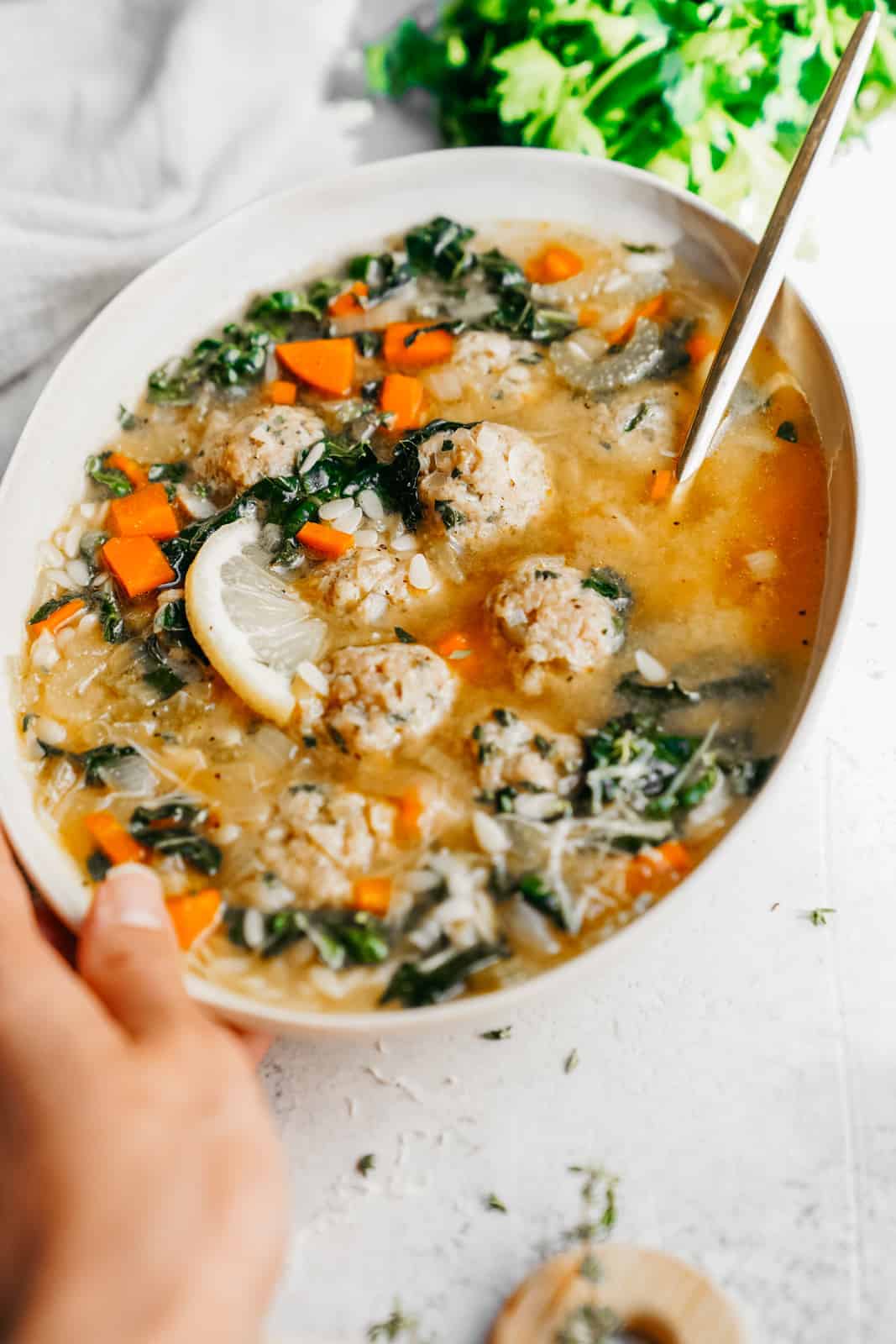 A bowl of Vegan Italian Wedding Soup with vegan meatballs, vegetables, and a slice of lemon served on a table.