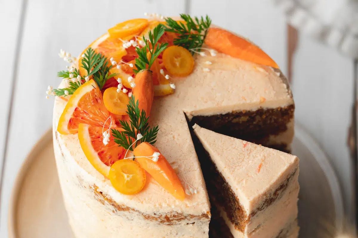 A citrus-flavored Easter cake with a slice removed, garnished with slices of orange and green herbs.
