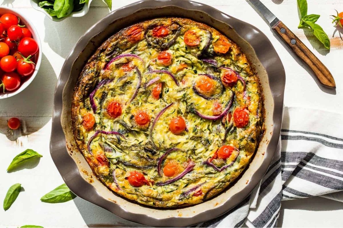 A spring quiche with tomatoes and onions in a pan.