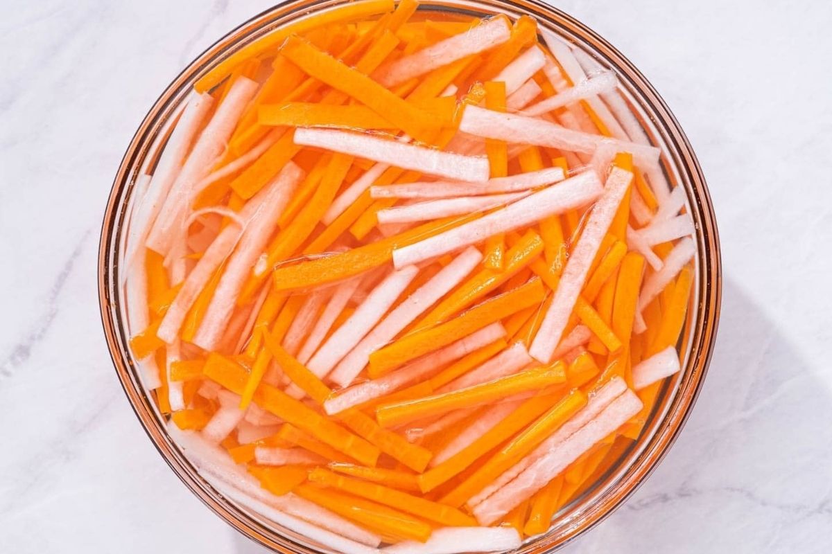 Bowl containing pickled julienned carrots and daikon radish.