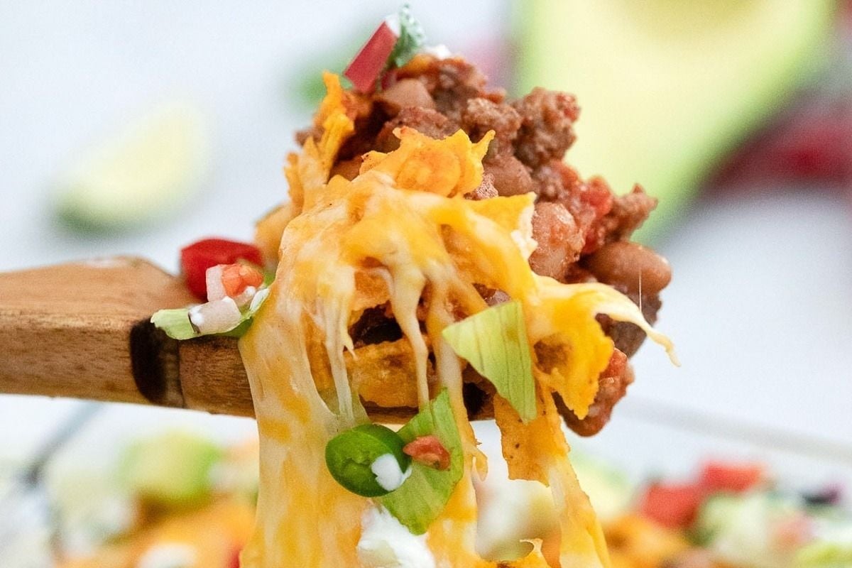 A wooden spoon is being used to pick up a bowl of Mexican nachos, perfect for potluck sides.