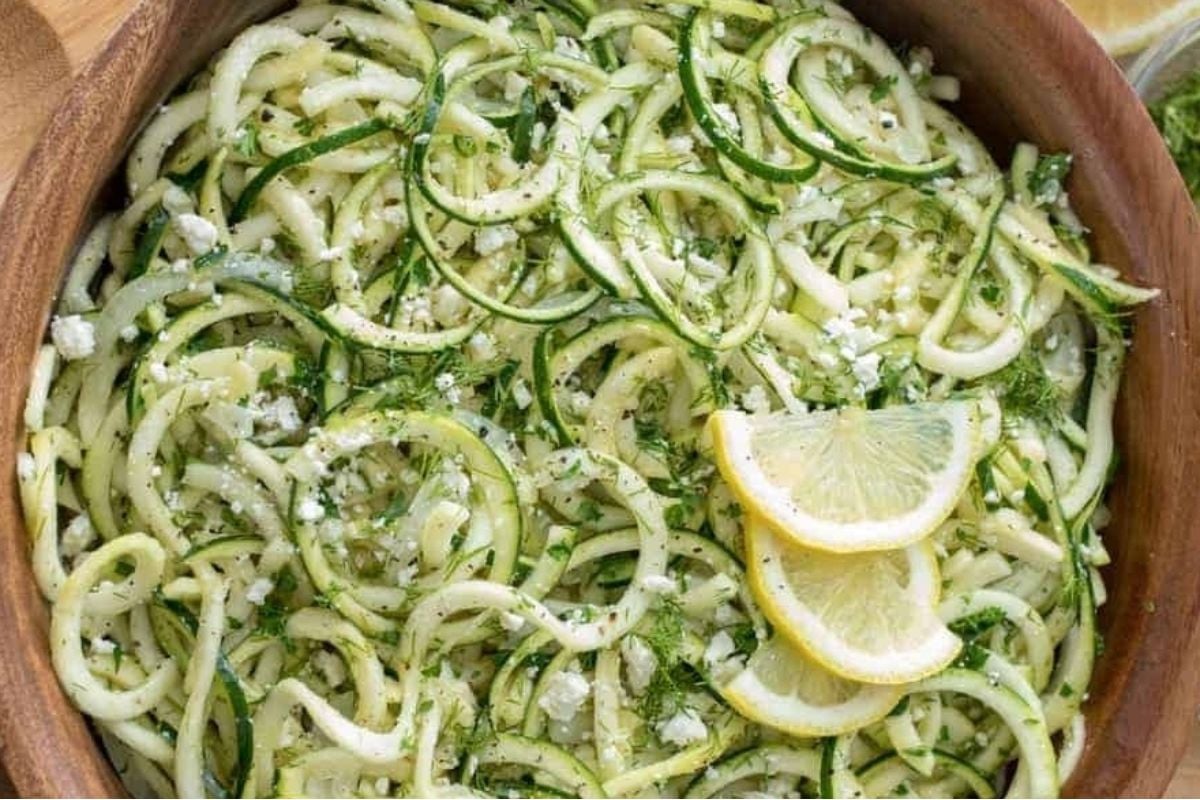Potluck sides: Zucchini noodles in a wooden bowl with lemon wedges.