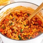 A pot full of American chop suey with a wooden spoon.
