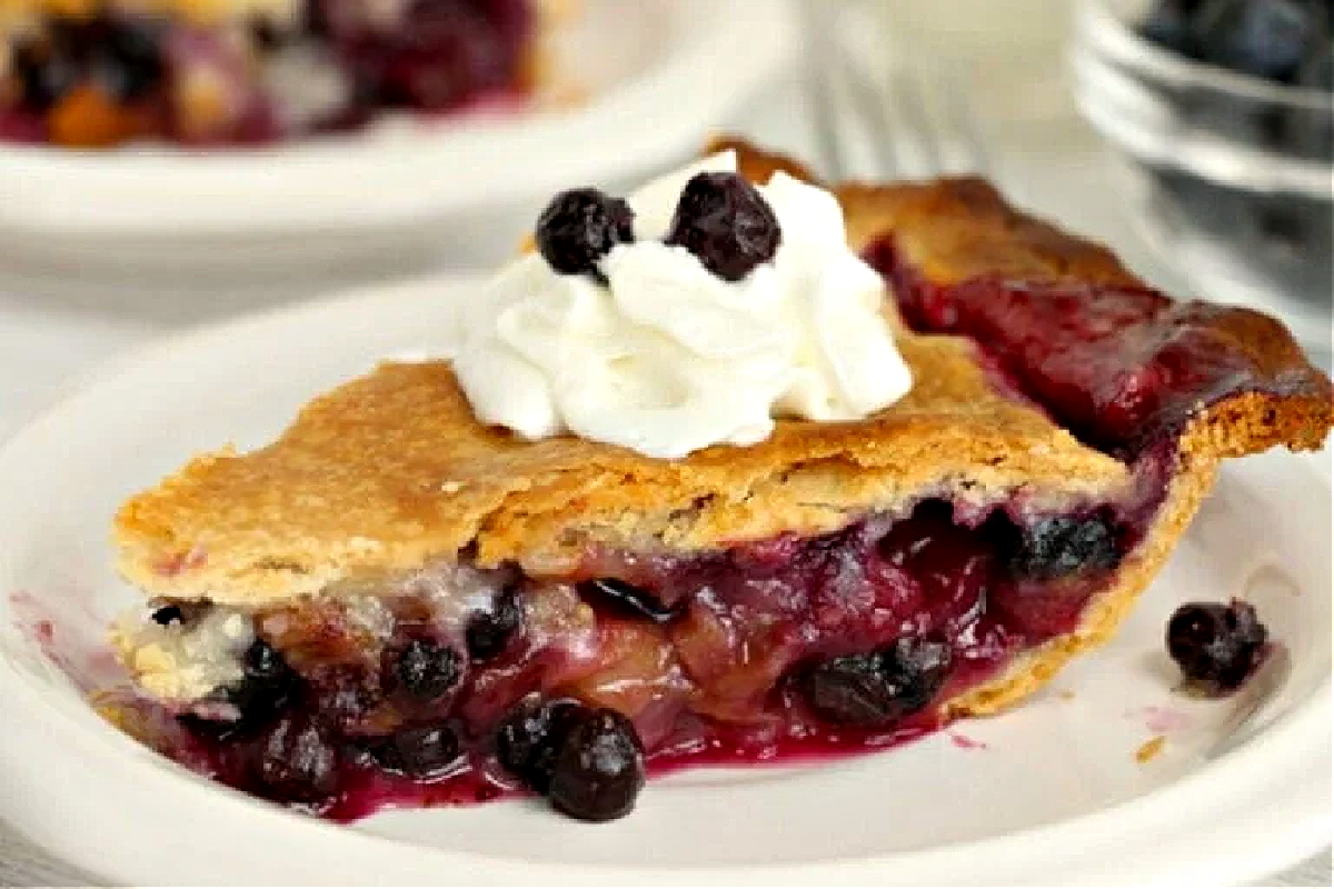 A slice of blueberry pie from our pie recipes, topped with whipped cream on a white plate.
