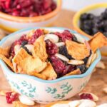 A bowl of coastal medley trail mix on a wooden surface with additional bowls of ingredients in the background.