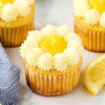 Lemon stuffed cupcakes with buttercream icing and lemon slices on a marble table.