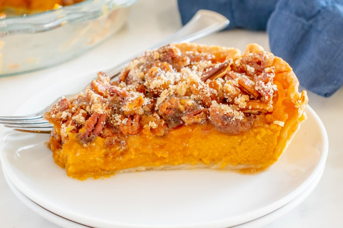 A slice of sweet potato pie with pecan topping from our pie recipes on a white plate.