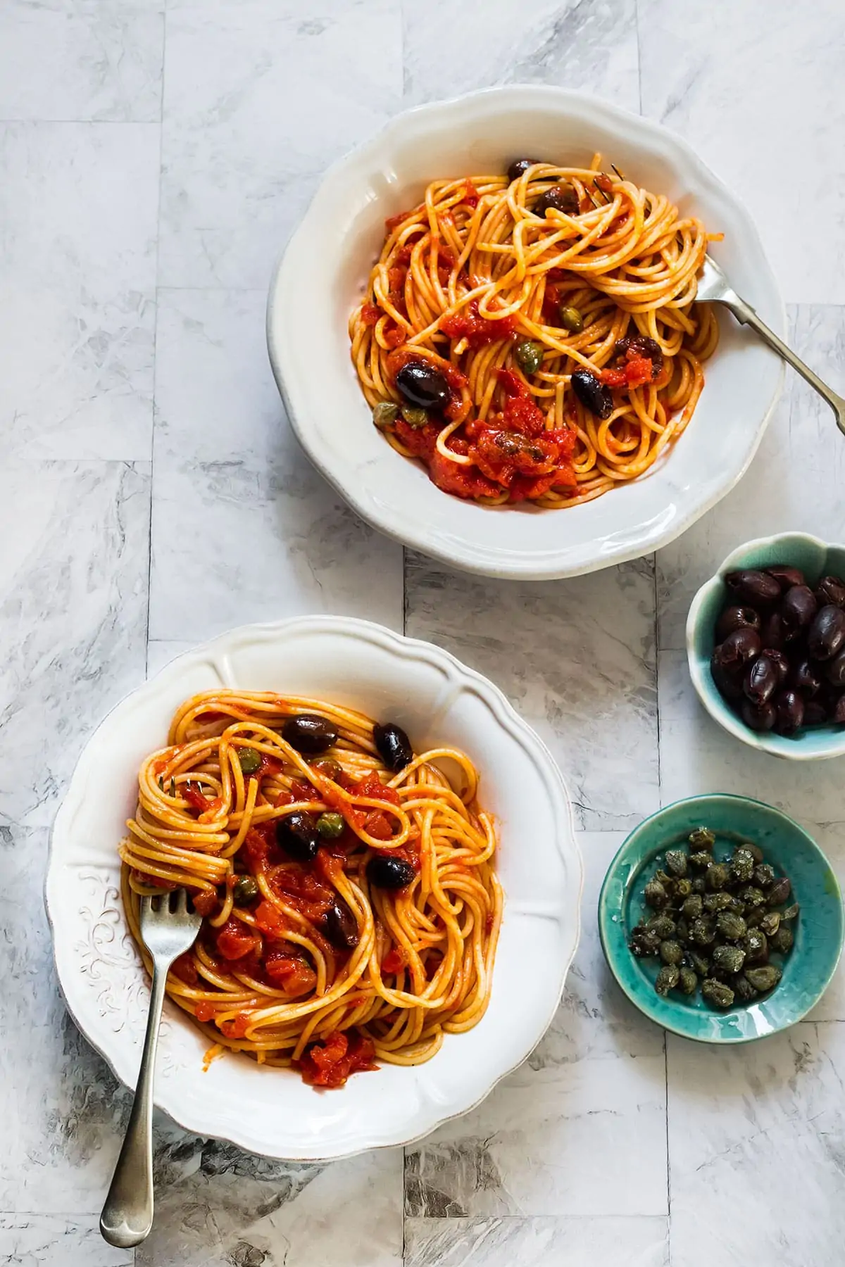 Two plates with spaghetti alla puttanesca seen from above.