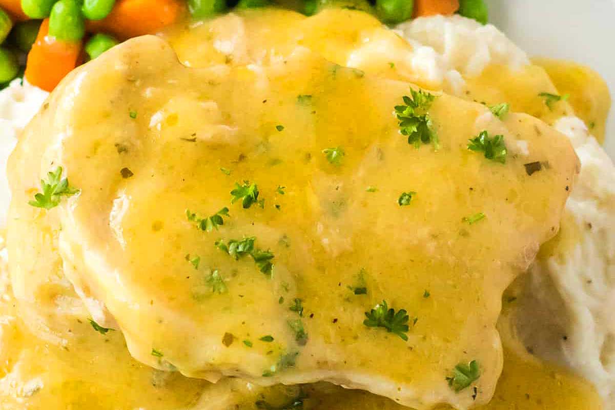Close-up of a pork chop dinner with mashed potatoes, gravy, and mixed vegetables, garnished with parsley.