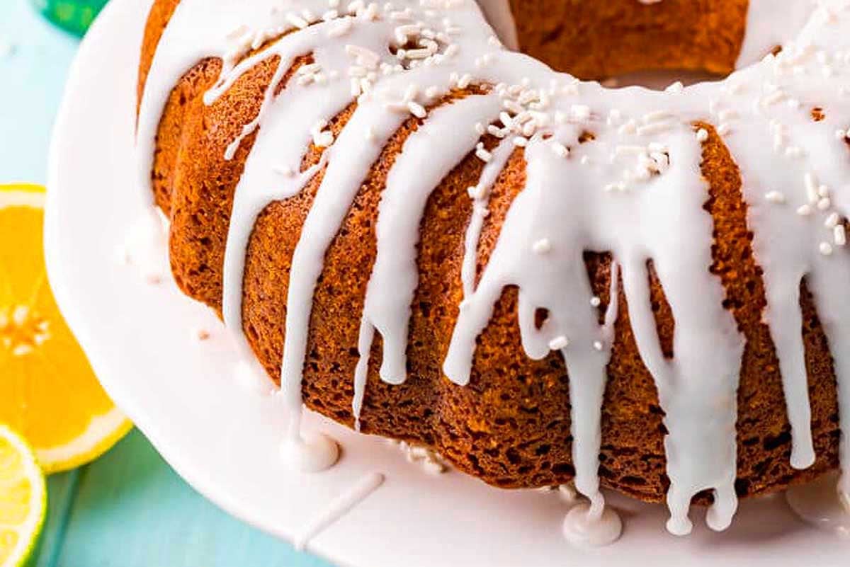 A lemon bundt cake with white glaze, sprinkles, and pudding mix on a plate.