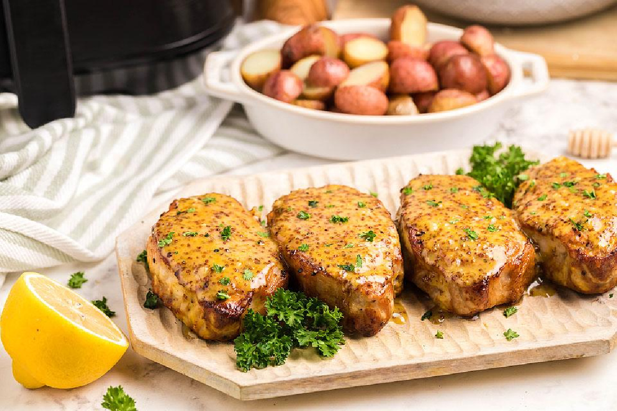 Grilled pork chop recipes garnished with parsley on a wooden board, served with a side of roasted potatoes and lemon slices.