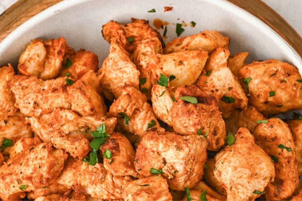 Cooked, seasoned chicken pieces garnished with chopped herbs and a hint of citrus, served in a white bowl—perfect for fans of Lemon Recipes.