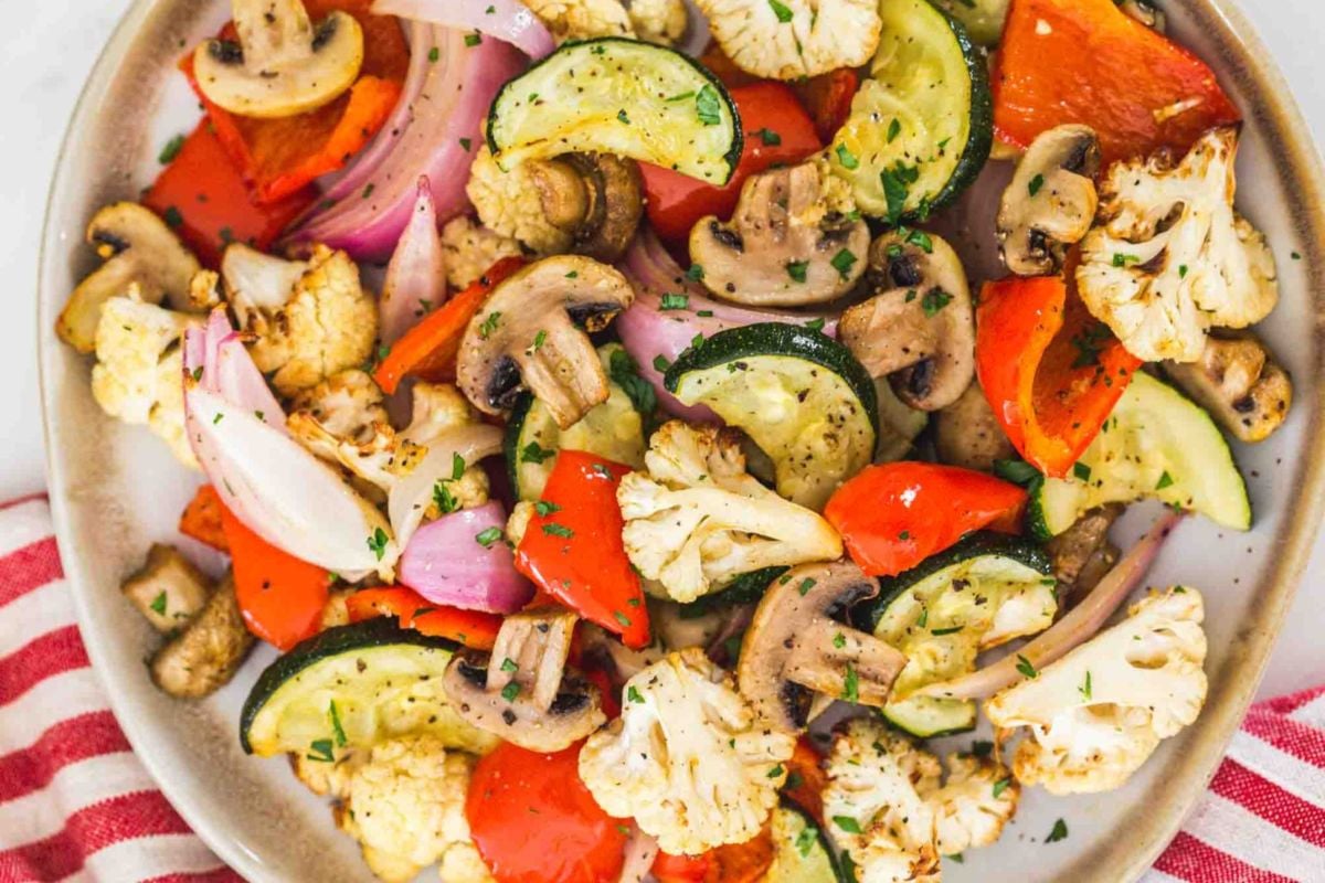 A plate of roasted vegetables, using frozen vegetables like cauliflower, zucchini, red bell pepper, onion, and mushrooms for a convenient and flavorful dish.
