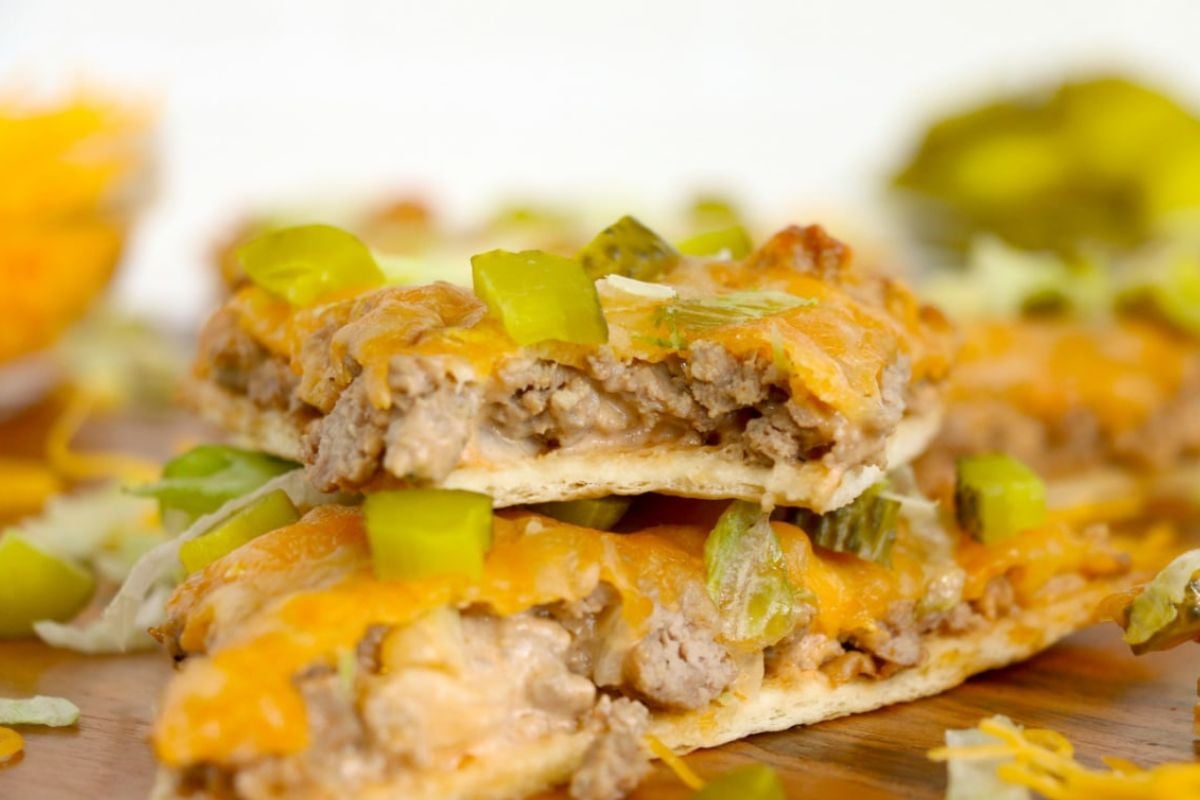 Close-up of two slices of a cheeseburger casserole topped with melted cheese, ground beef, chopped green bell peppers, and pickles, placed on a wooden surface. Perfect for fans of hearty meal ideas or those exploring delicious ketchup recipes.