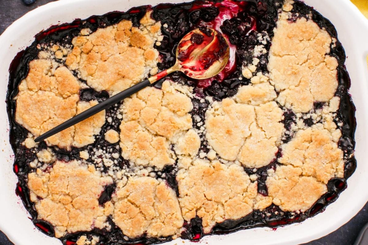 A freshly baked blueberry cobbler from our Blueberry Recipes collection in a white baking dish with a serving spoon.