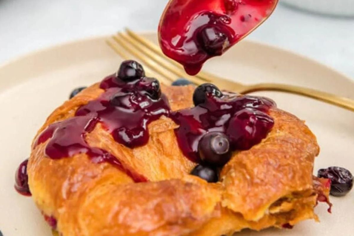 Blueberry Recipes compote being poured onto a golden-brown pancake on a plate.