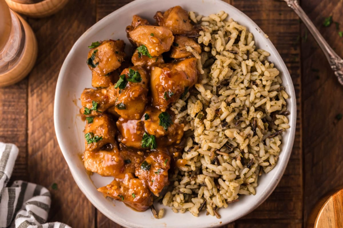 A plate of chicken dinners in sauce with a side of herbed rice.