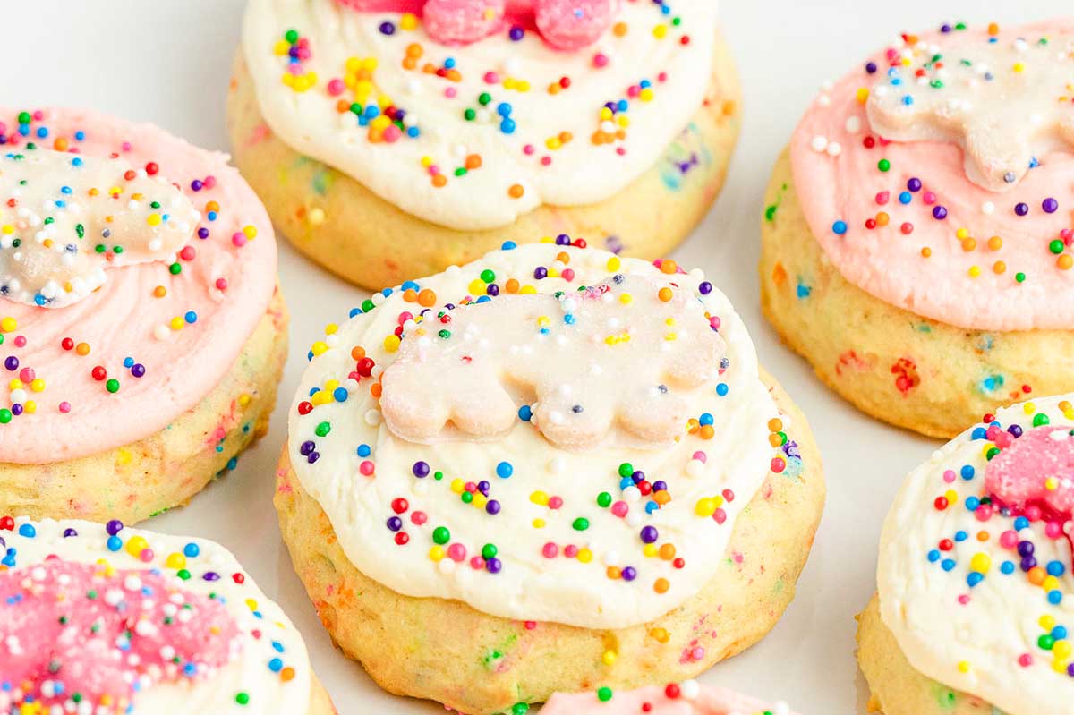 A close-up of several sugar cookies topped with pastel-colored frosting and multi-colored sprinkles, inspired by recipes that use circus animal cookies.