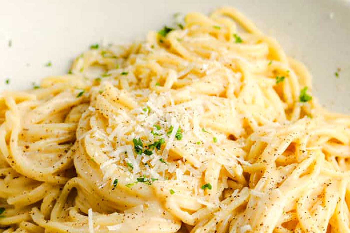 A close-up image of spaghetti seasoned with grated parmesan cheese, black pepper, and finely chopped herbs, prepared in 30 minutes or less.