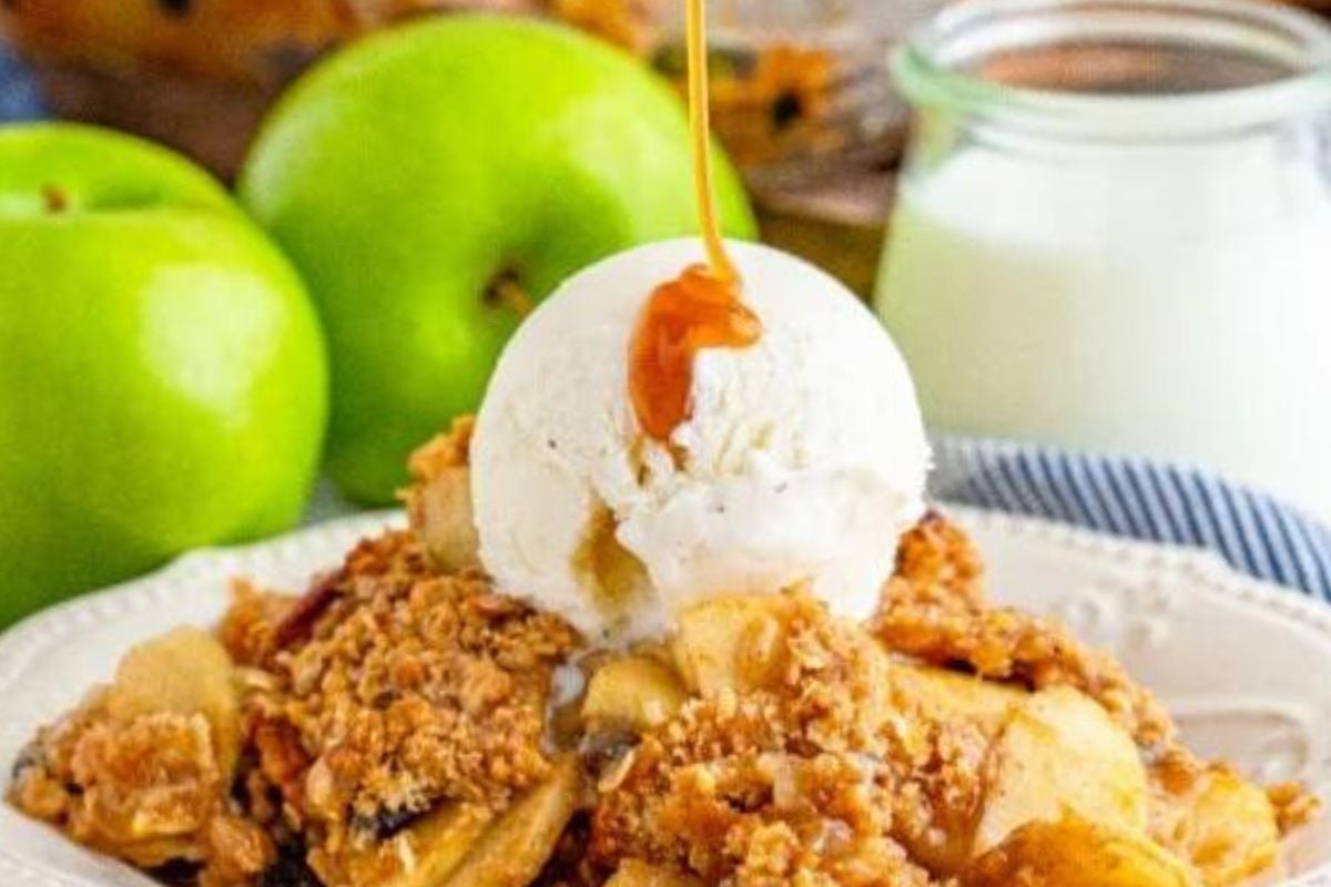 A scoop of vanilla ice cream melting over warm apple crumble, with caramel recipes fresh apples and a glass of milk in the background.