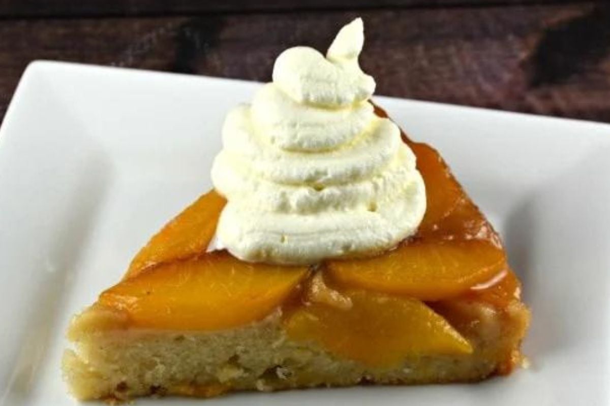 A slice of peach tart topped with caramel whipped cream on a white plate.