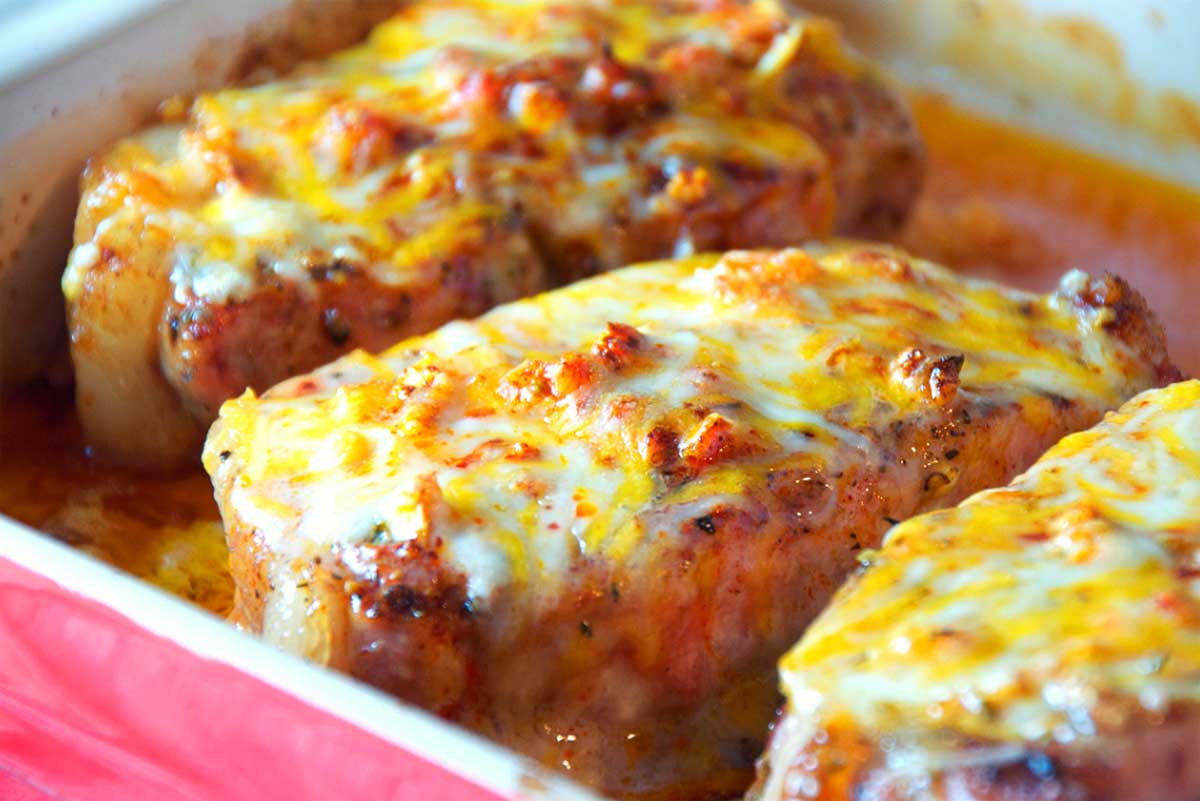 Golden-brown pork chops topped with melted cheese and tomato sauce in a baking dish.