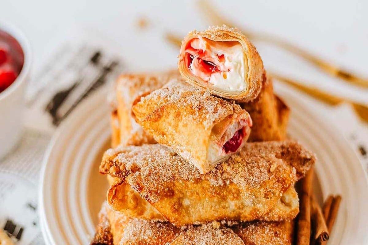 Crispy cherry cheesecake filled egg rolls stacked on a white plate.
