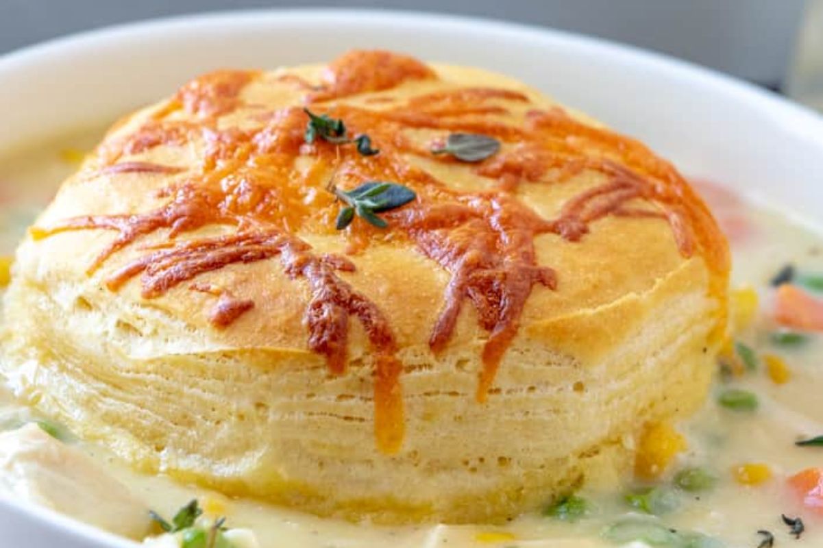 A close-up of a fluffy, layered soufflé topped with melted cheese and herbs, served in a white bowl with a can of cream soup and vegetables.