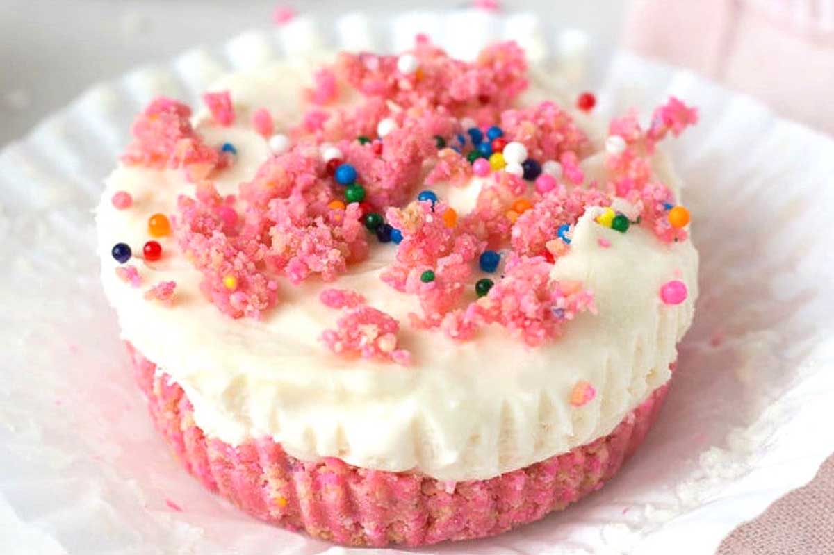 A pink rice crispy treat topped with white icing and colorful sprinkles, inspired by recipes that use circus animal cookies, on a white napkin.