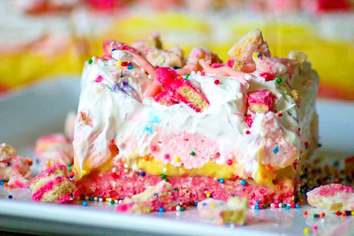 A colorful, multilayered dessert topped with whipped cream, sprinkles, and circus animal cookies, served on a white plate.