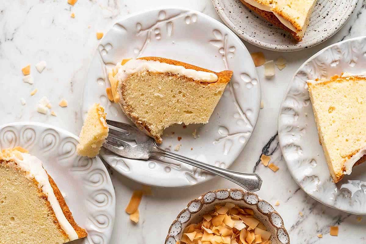 Slices of iced pound cake with pudding mix on decorative plates with a fork and scattered coconut flakes.