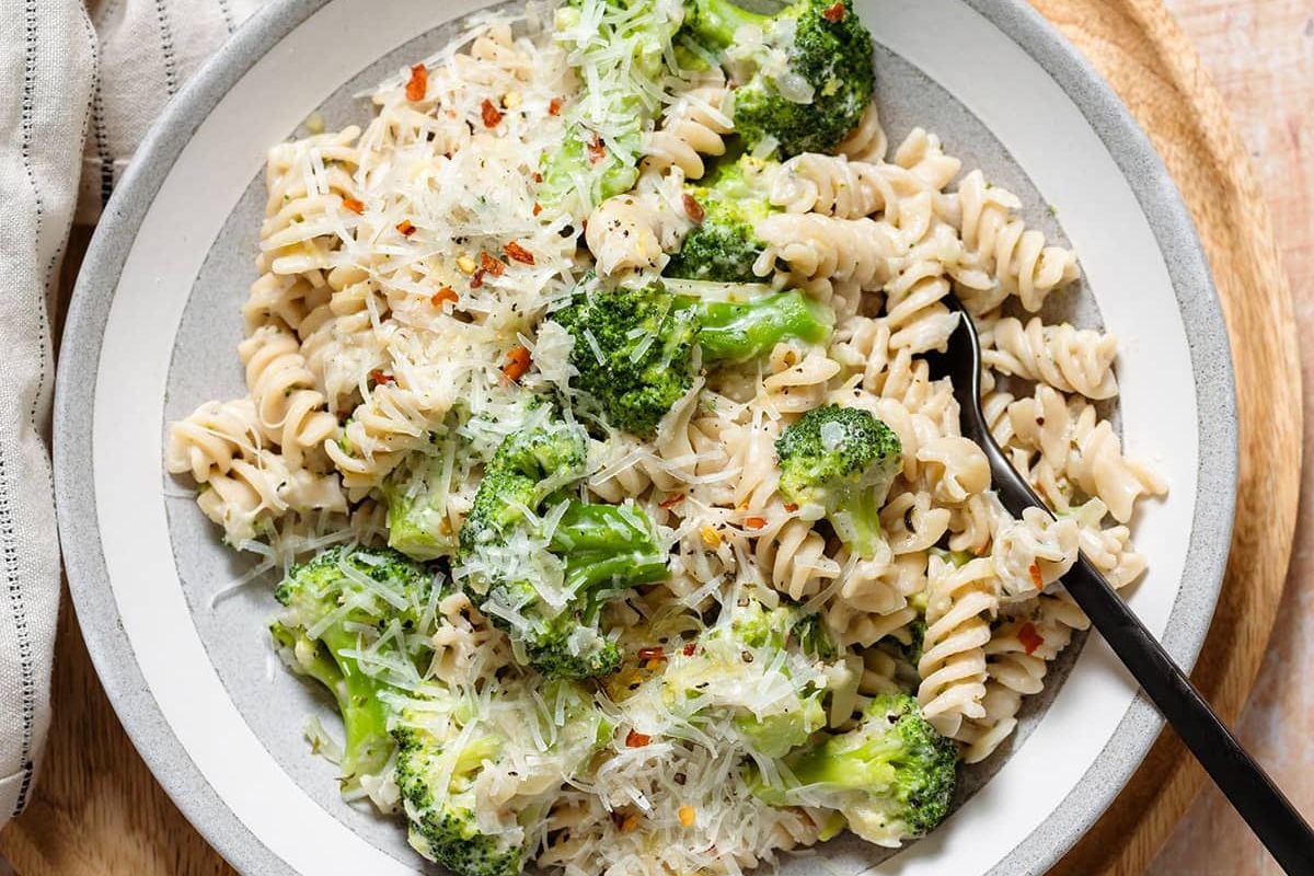A plate of rotini pasta with broccoli—using frozen vegetables—grated cheese, and a black fork on the side.