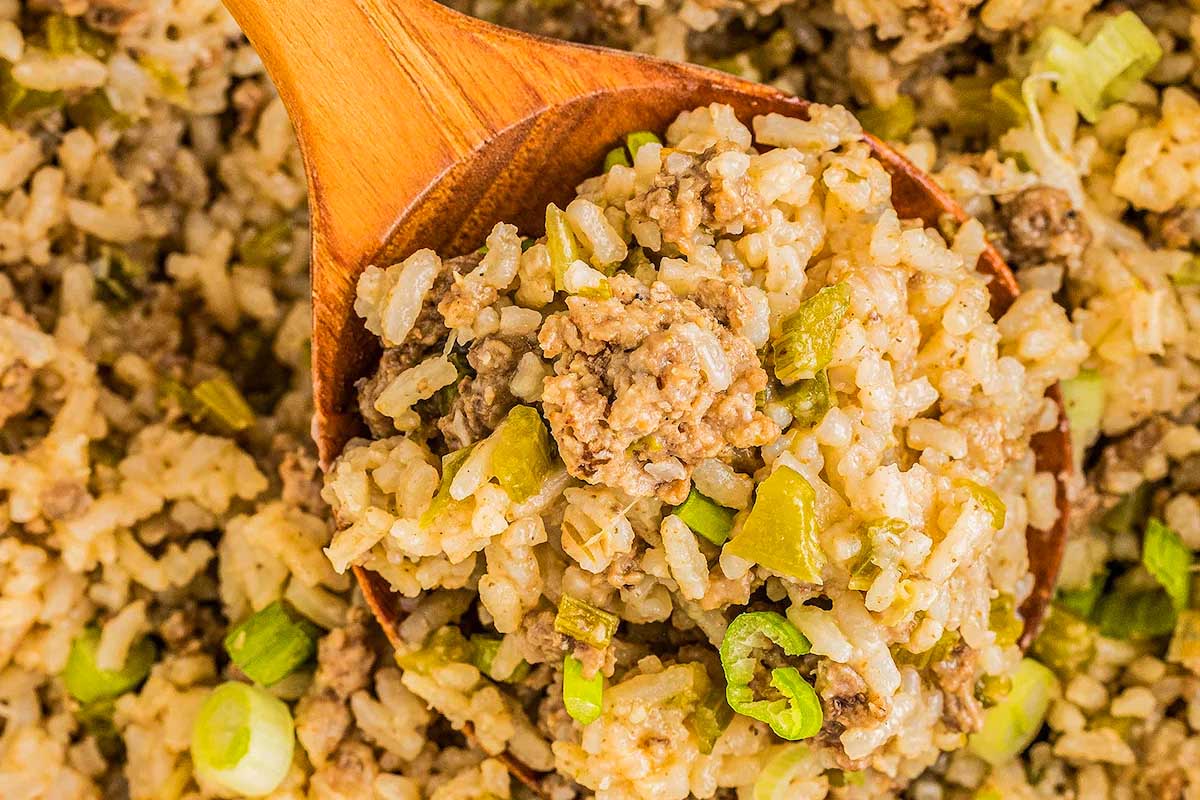 A wooden spoon scooping up a serving of cooked dirty rice with ground meat, green bell peppers, and scallions, prepared in 30 minutes or less.