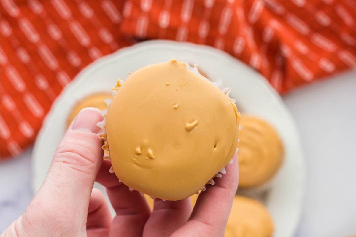 A hand holding a caramel-dipped cake or cookie with more treats visible in the background.
