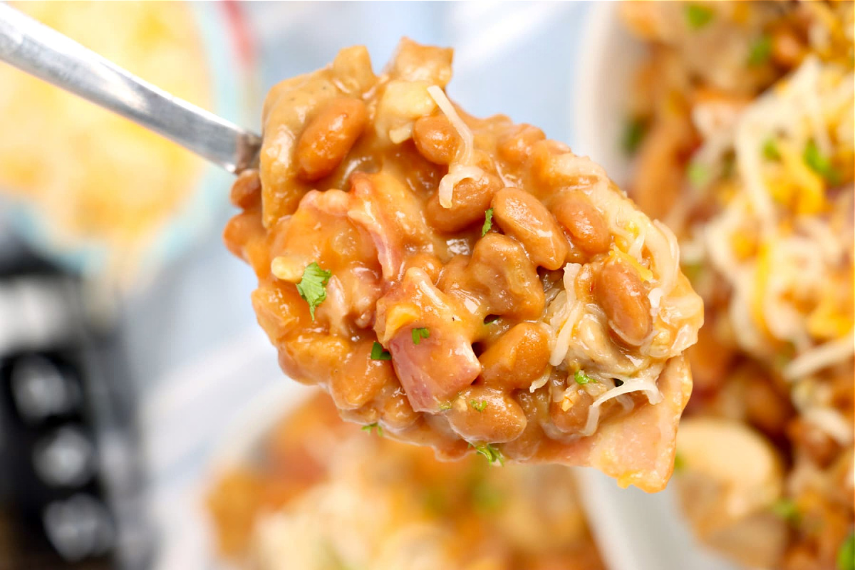 A close-up of a spoonful of baked beans with melted cheese, indicative of a hearty and cheesy chicken dinners dish.