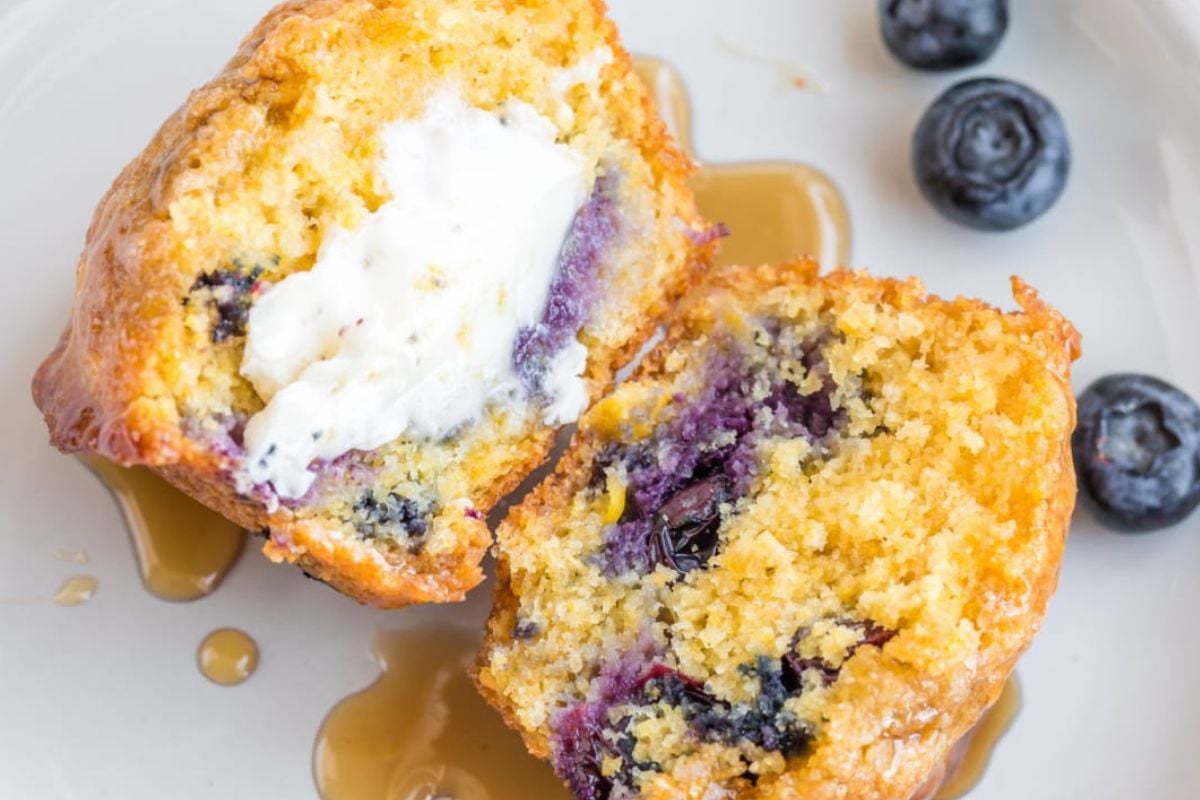 A split blueberry muffin with a pat of butter melting inside, drizzled with honey, accompanied by fresh blueberries from our Blueberry Recipes collection.