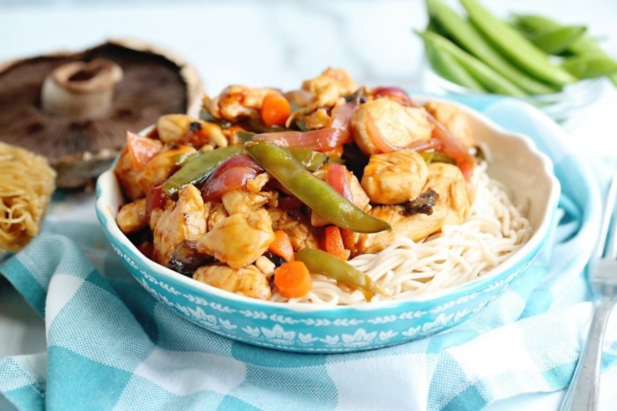 A bowl of stir-fried chicken dinners and vegetables served over noodles.