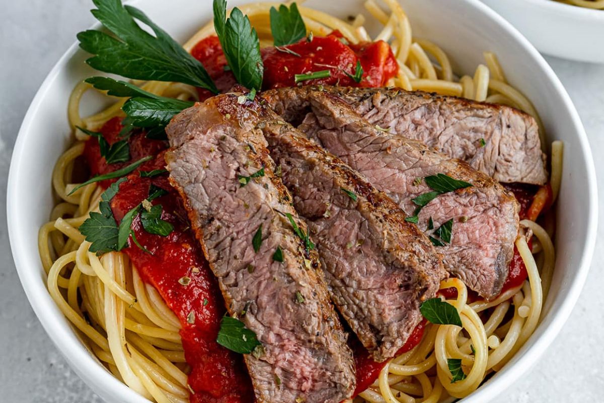 Sliced steak served over spaghetti with tomato sauce and garnished with parsley, as part of recipes featuring noodles.