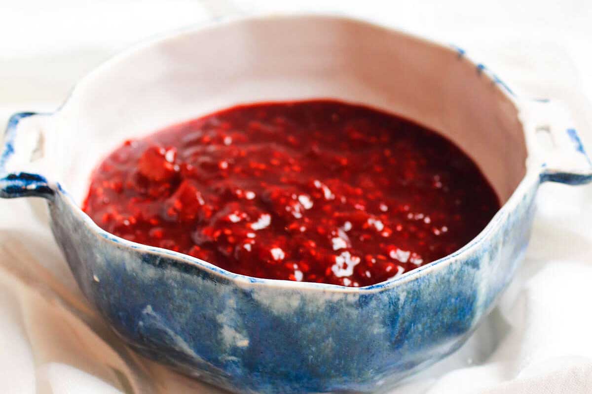 Blue ceramic pot filled with bright red rhubarb jam on a white cloth.