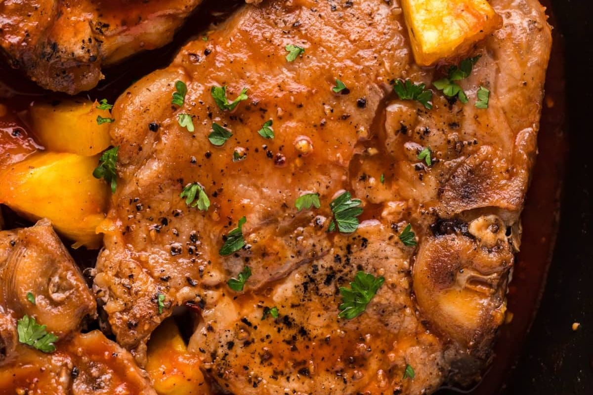 Close-up of braised pork chop with sauce, garnished with parsley, in a skillet.