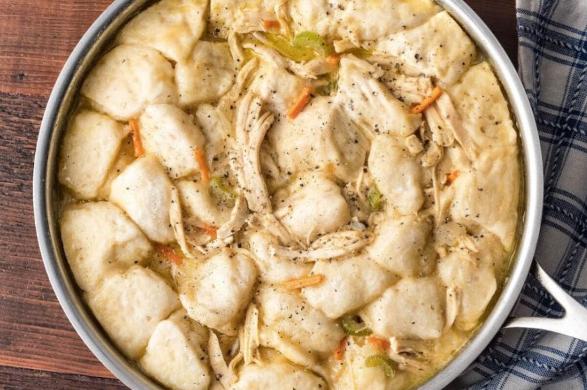 A pot of chicken and dumplings, featuring shredded chicken and large dumplings in a creamy broth made with a can of cream soup, garnished with carrots and celery.