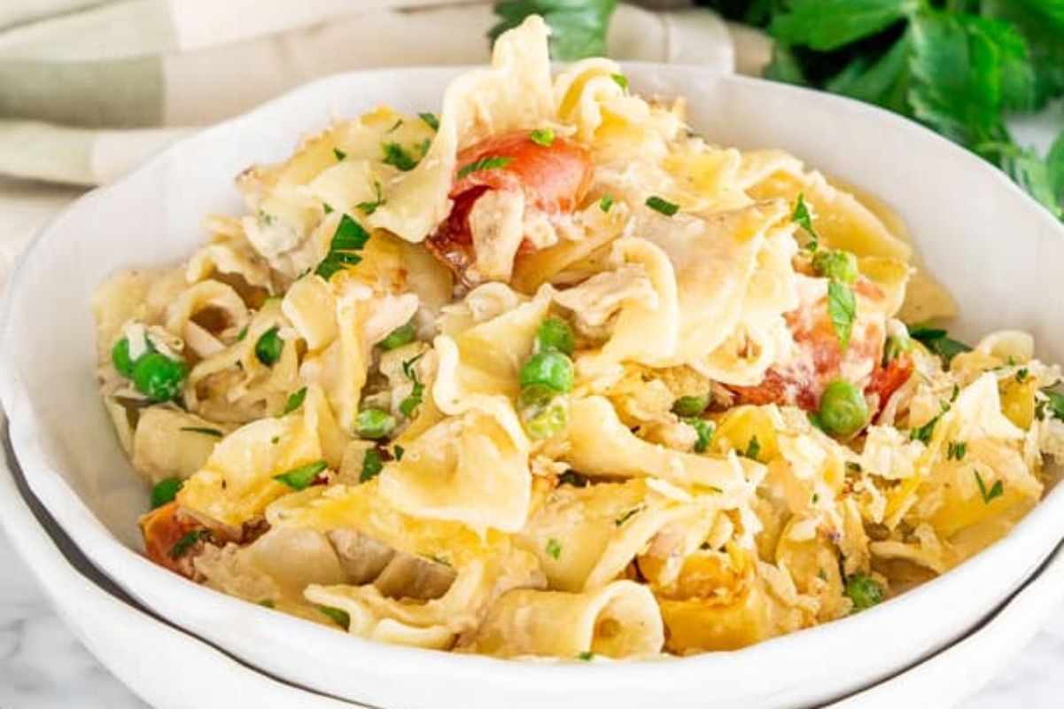 A bowl of creamy pasta with peas, carrots, and shredded cheese, made with a can of cream soup, garnished with parsley on a marble countertop.