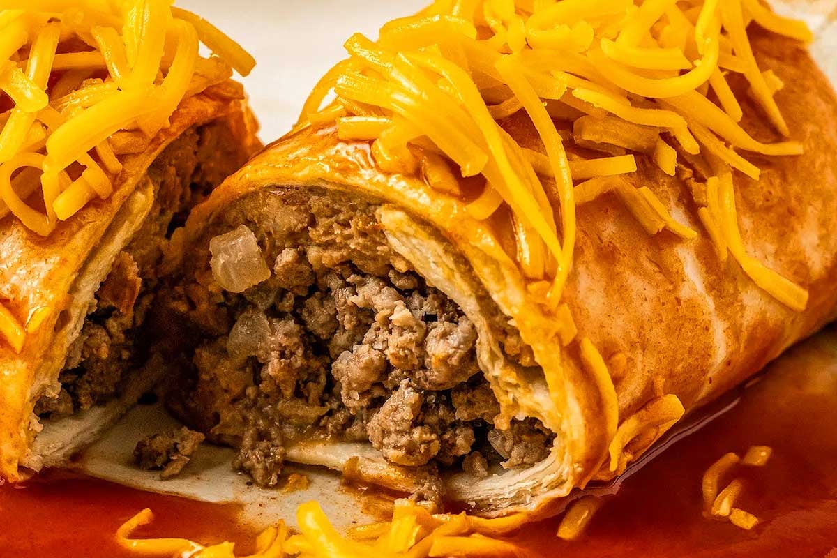 Close-up of a sliced burrito inspired by Taco Bell, topped with shredded cheddar cheese, showing a filling of seasoned ground beef and onions.