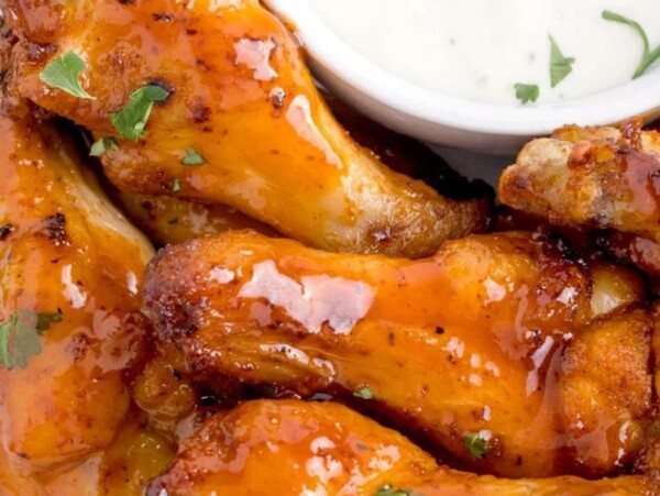 Close-up of glazed buffalo chicken wings garnished with herbs next to a small cup of ranch dressing—perfect for those craving quick and easy air fryer dinner recipes.