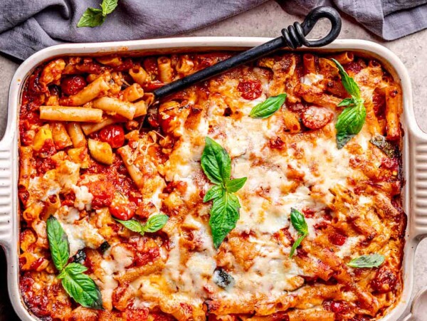Baked ziti casserole in a 9x13 baking dish, garnished with basil leaves, featuring melted cheese and tomato sauce.