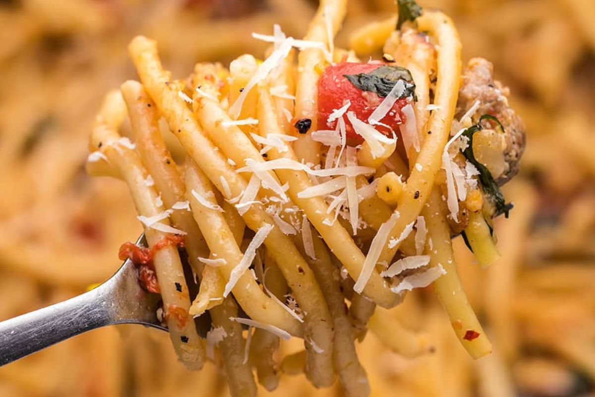 A fork lifting spaghetti with tomato, basil, and grated cheese from recipes featuring noodles.