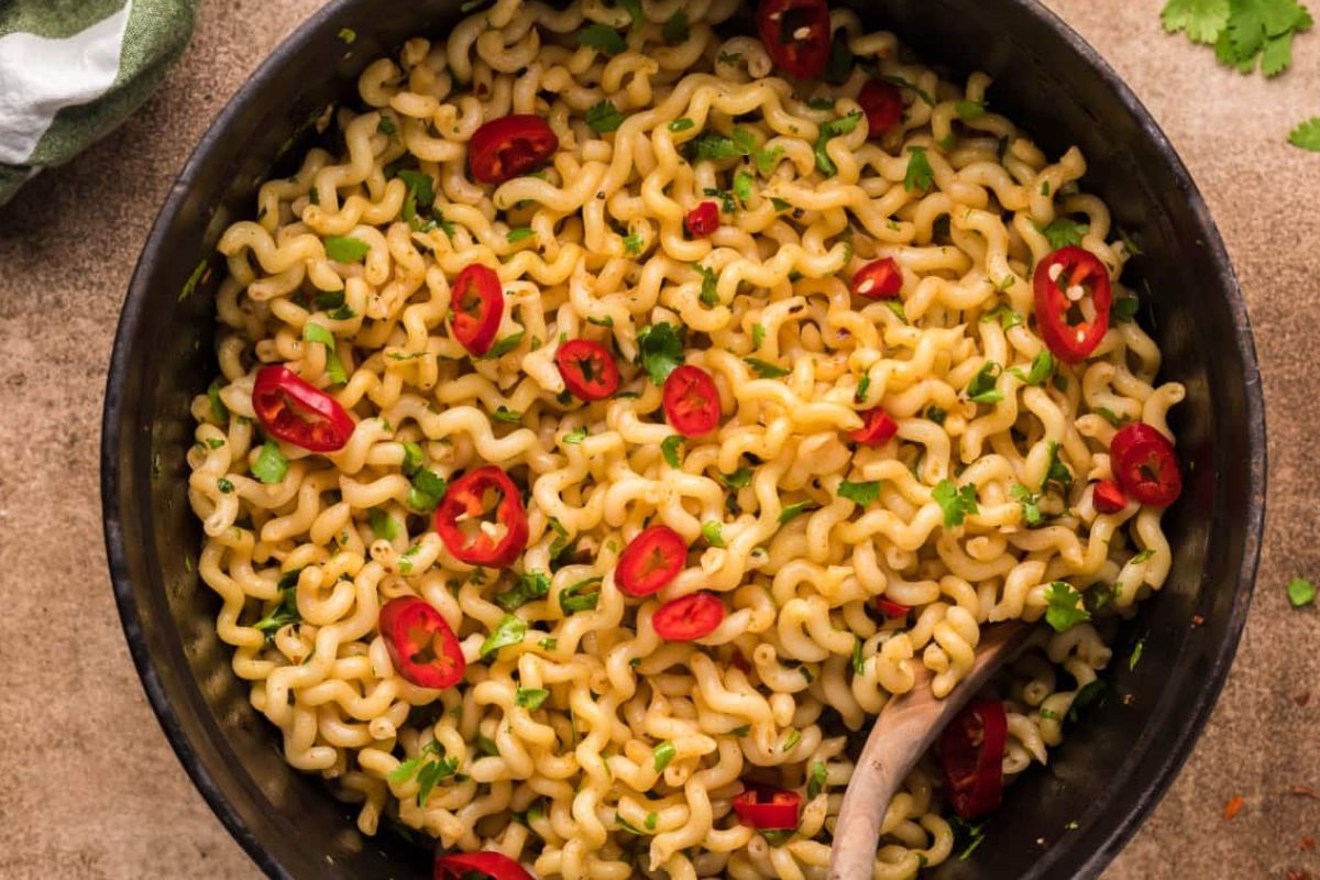 A bowl of spicy noodle dish from our recipes featuring noodles, garnished with sliced red chilies and herbs.