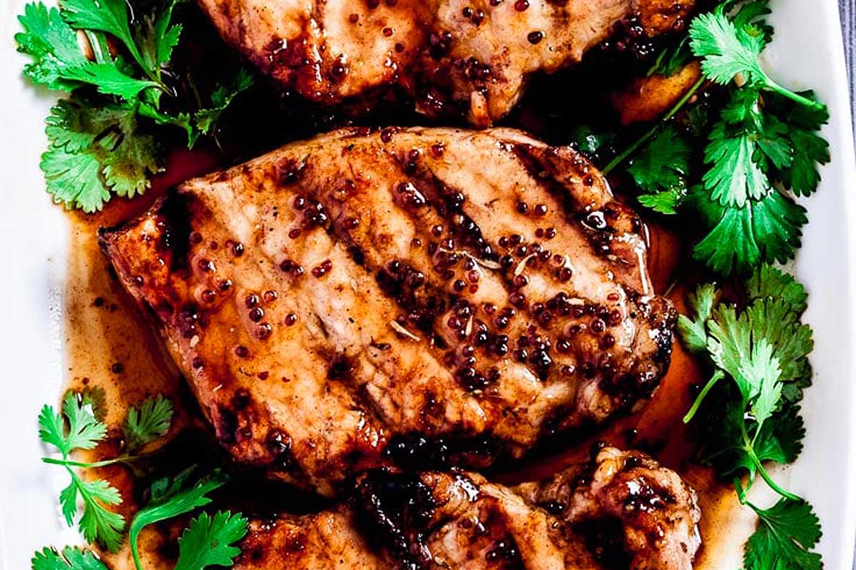 Grilled pork chops seasoned with herbs and coated in a peppercorn sauce, garnished with fresh parsley on a white plate.