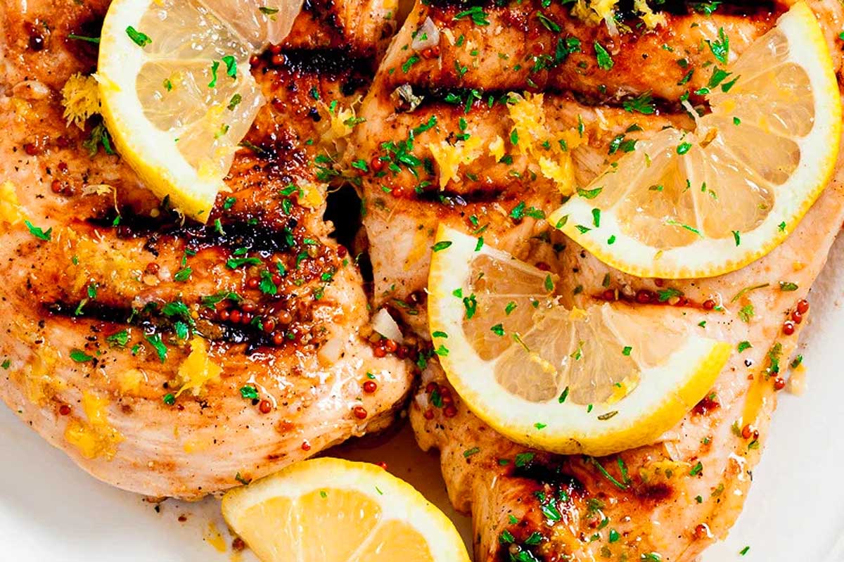 Grilled chicken breasts topped with lemon slices and herbs on a white plate, prepared in 30 minutes or less.