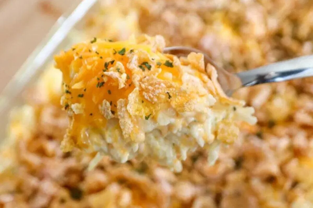 A close-up image of a fork lifting a serving of cheesy potato casserole with a crispy top, made with a can of cream soup, and garnished with herbs.